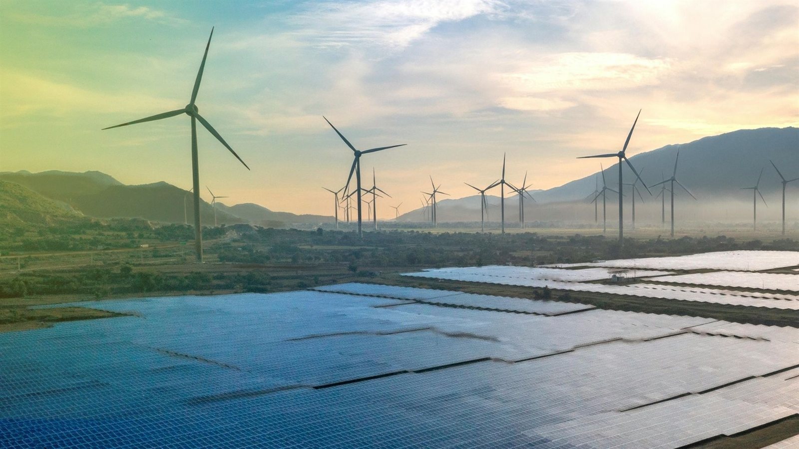 Campo fotovoltaico e turbine eoliche al tramonto, a illustrare la produzione rinnovabile nel modello operativo del reseller.